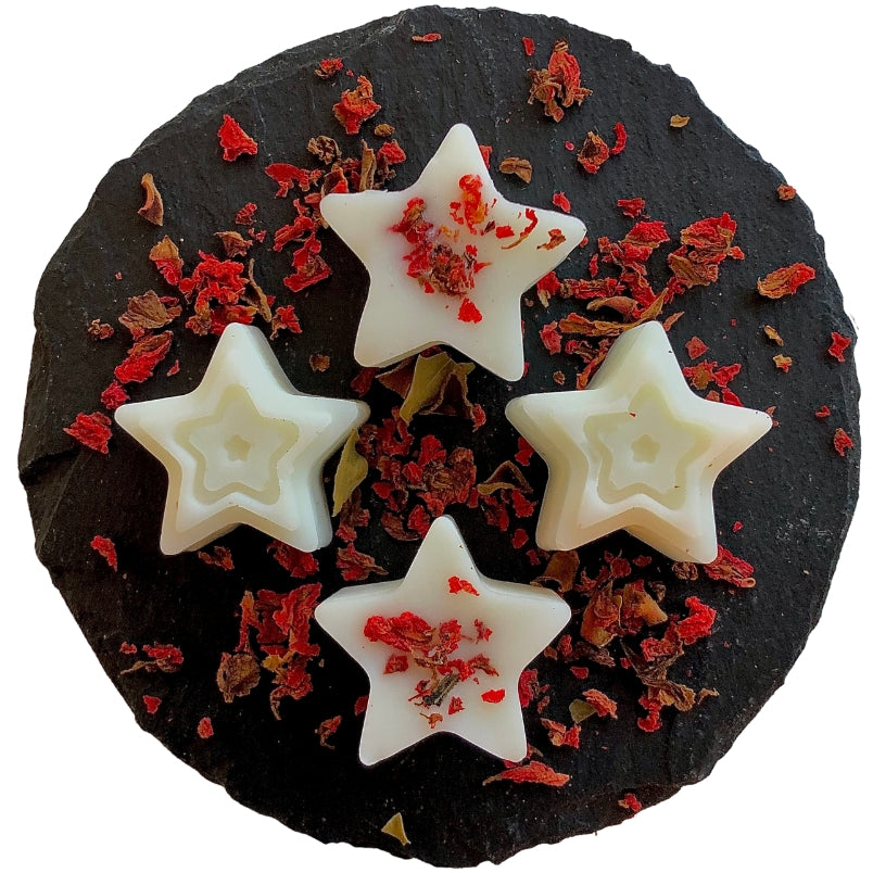 Four star shaped black pomegranate scented wax melts with red pomegranate flowers on a circular slate.