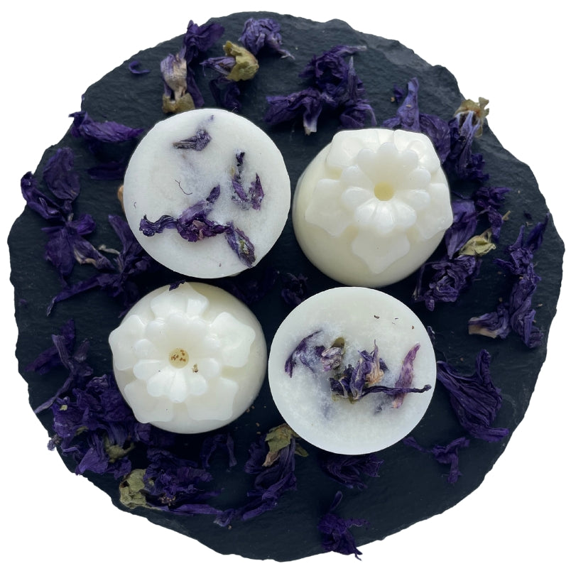 Four petal shape botanical wax melts with blue mallow decoration on a circular slate.