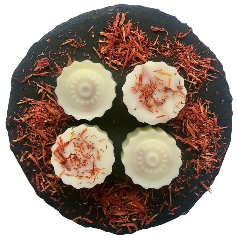 Four mandarin and sandalwood wax melts arranged on a grey slate decorated with red safflowers.