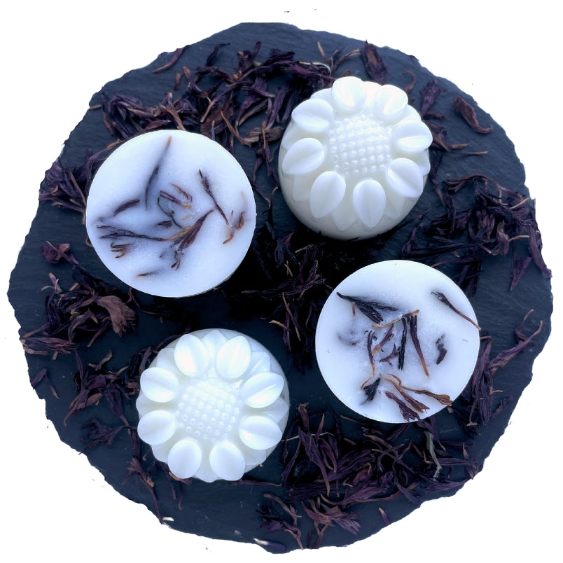 Four sunflower-shaped bergamot and white musk wax melts on a slate with purple cornflowers.