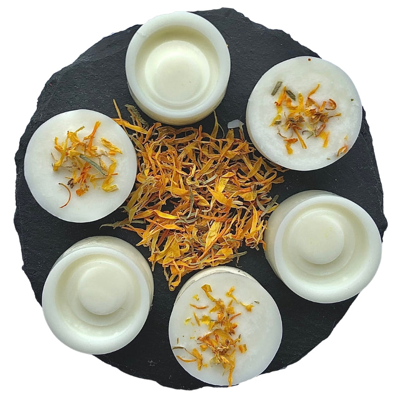 Six swirl shaped lemongrass and ginger wax melts with marigold botanicals on a circular slate.