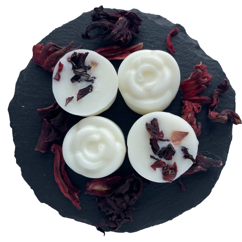 Four rose shaped botanical wax melts with hibiscus rose on a circular slate.