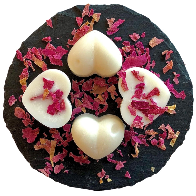 Four heart shaped rose and oud scented wax melts with peony botanicals sitting on a circular slate