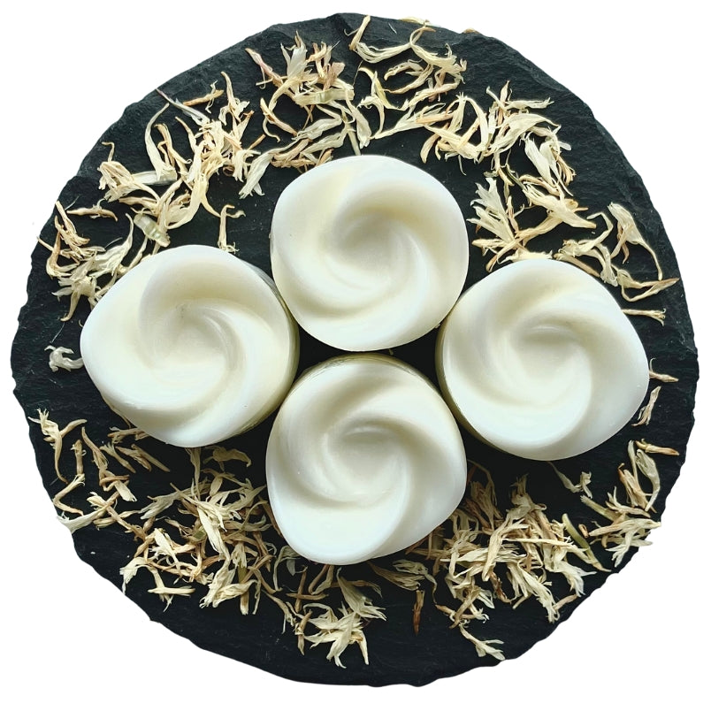 Four swirl-shaped Vanilla Sands wax melts arranged on a circular grey slate decorated with white cornflowers.