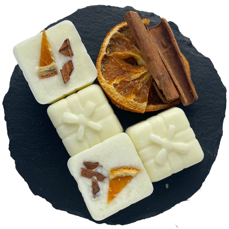 Four cinnamon and orange Yuletide wax melts on a circular slate with dried orange and cinnamon sticks.